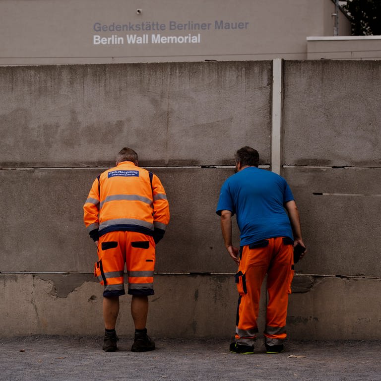 Zwei Männer schauen auf dem Gelände der Gedenkstätte Berliner Mauer an der Bernauer Straße durch eine Mauerritze auf ein Reststück der ehemaligen Grenzanlage. Sie ist Teil der Gedenkstätte Berliner Mauer. (Foto: dpa Bildfunk, picture alliance/dpa | Paul Zinken)