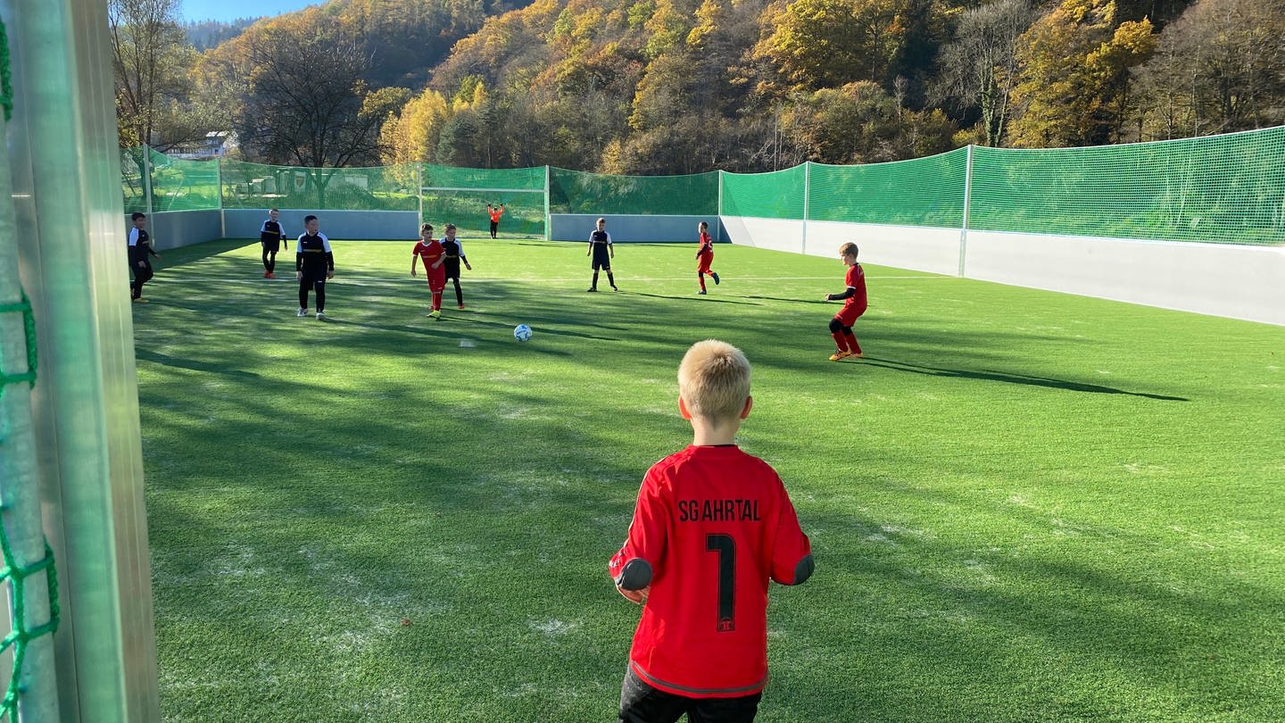 Kinder in roten und schwarzen Trikots spielen auf Fußball-Kleinfeld.