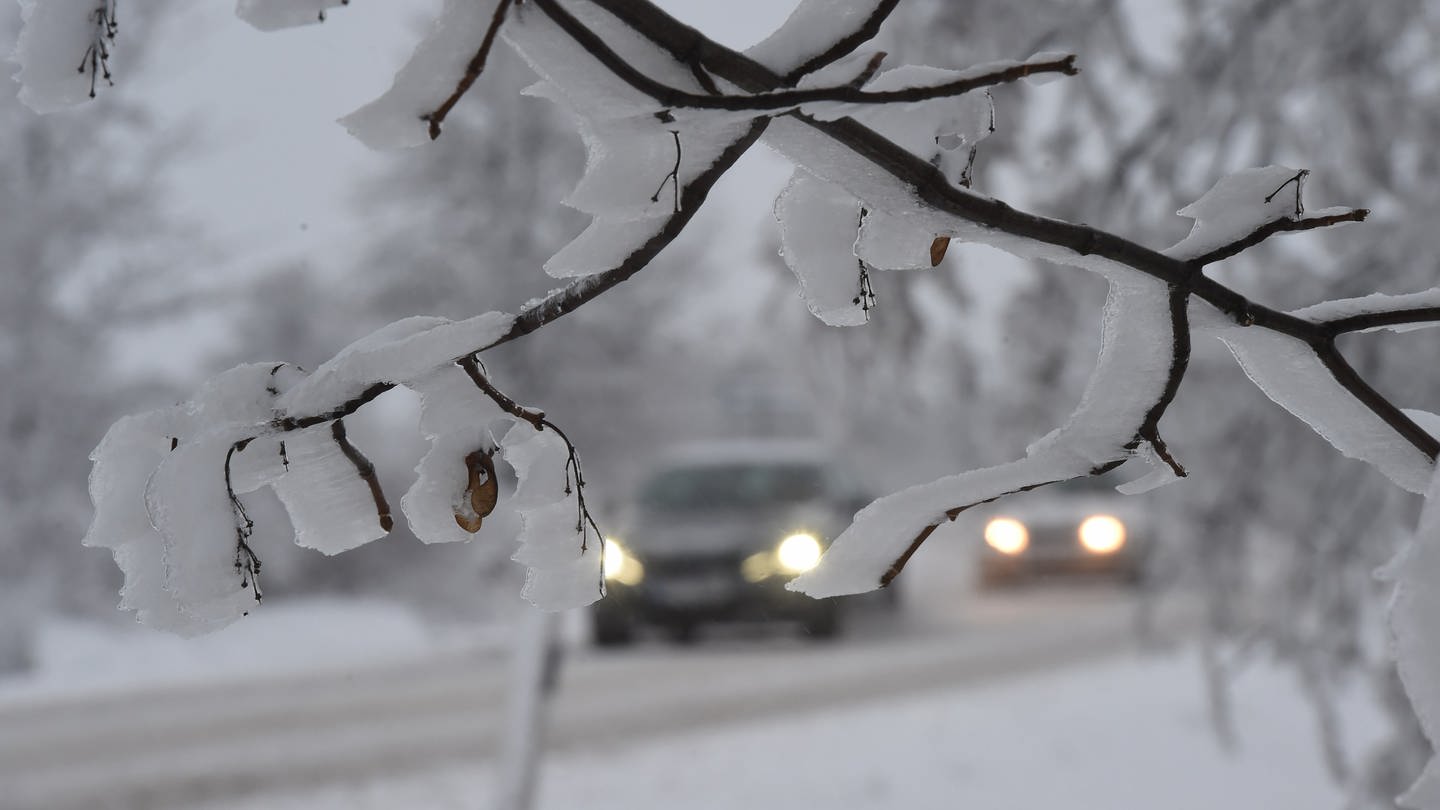 Autos fahren mit eingeschaltetem Licht über eine verschneite Straße.