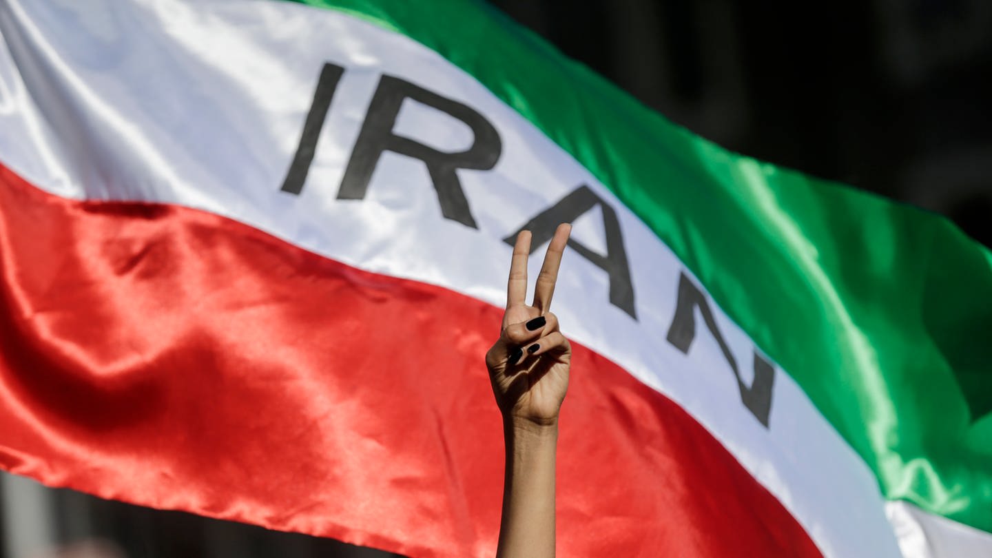 Eine Frau zeigt auf einer Demonstration iranischer Studenten für die Menschenrechte im Iran das Victory-Zeichen vor einer iranischen Fahne. Auslöser der Demonstration war der Tod der 22-jährigen Mahsa Amini im Iran, nachdem sie von der Sittenpolizei wegen ihres angeblich «unislamischen Outfits» festgenommen wurde. (Foto: dpa Bildfunk, picture alliance/dpa/LaPresse via ZUMA Press | Cecilia Fabiano)