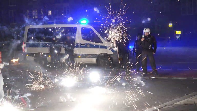 Polizeibeamte stehen hinter explodierendem Feuerwerk. Nach Angriffen auf Einsatzkräfte in der Silvesternacht hat die Diskussion um Konsequenzen begonnen. (Foto: dpa Bildfunk, picture alliance/dpa/TNN | Julius-Christian Schreiner)