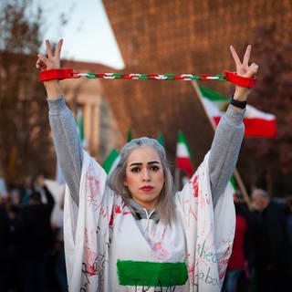 Frau auf Iran-Demo zeigt Peace Zeichen und hat ihre Hände aneinander gekettet (Foto: DASDING, picture alliance/dpa/SOPA Images via ZUMA Press Wire | Allison Bailey)