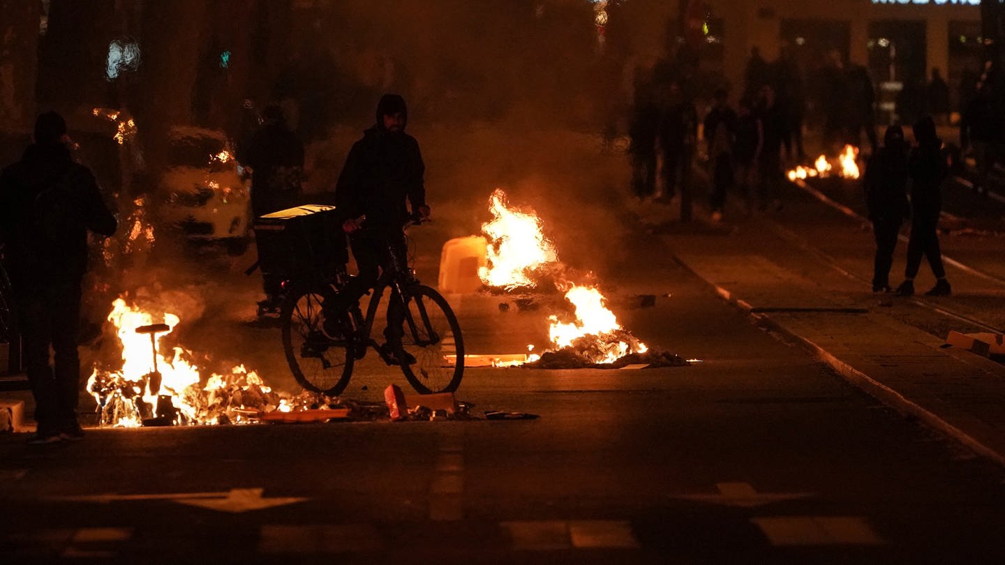Brennende Gegenstände sind nach den Protesten gegen die umstrittende Rentenreform auf einer Straße zu sehen (Foto: dpa Bildfunk, picture alliance/dpa/AP | Laurent Cipriani)
