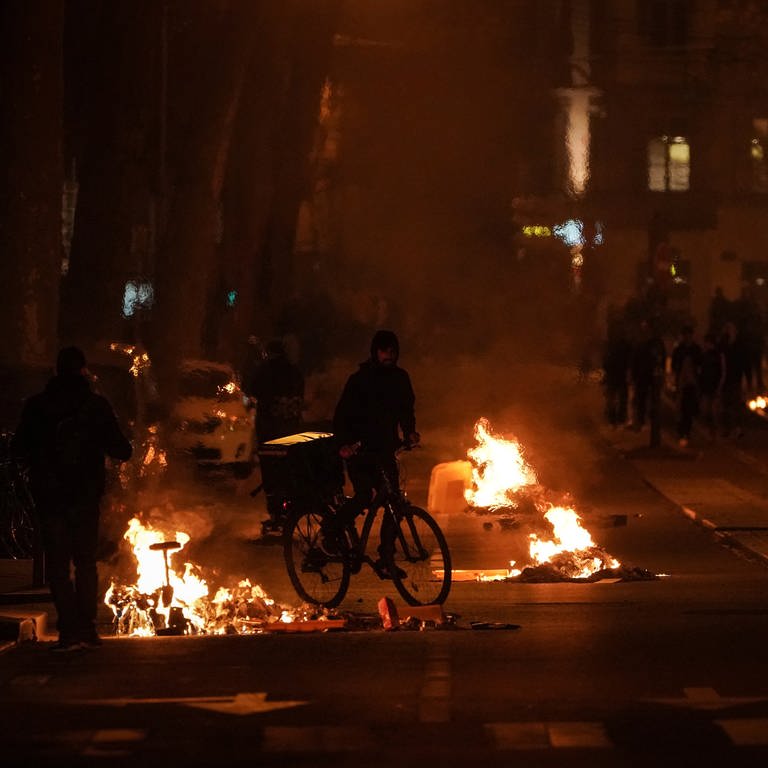 Brennende Gegenstände sind nach den Protesten gegen die umstrittende Rentenreform auf einer Straße zu sehen (Foto: dpa Bildfunk, picture alliance/dpa/AP | Laurent Cipriani)