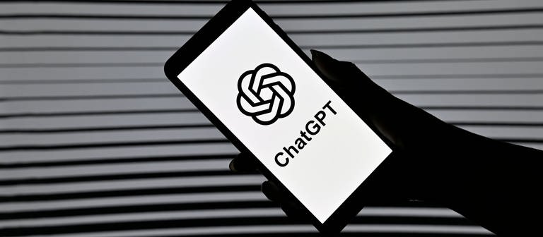 Smartphone in einer Hand mit dem ChatGPT Logo (Foto: IMAGO, IMAGO / Panama Pictures)