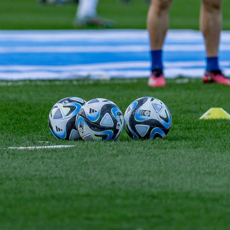 Smybolbild Fußball Frankfurt: Drei Fußbälle sind auf einem Fußballfeld zu sehen. (Foto: DASDING, IMAGO / Beautiful Sports)