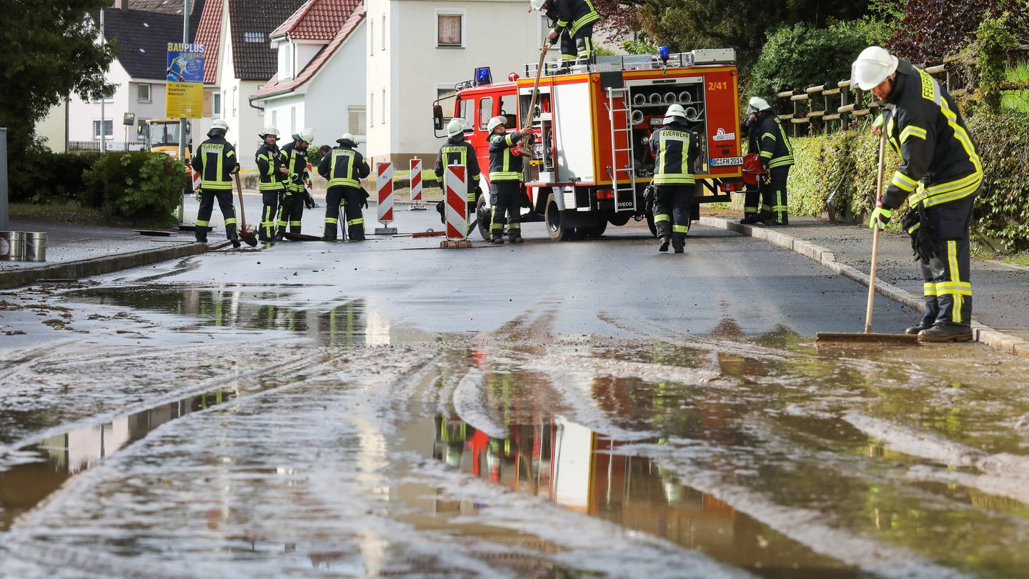 Feuerwehrleute reinigen eine vom Starkregen überflutete und verschmutzte Straße - Unwetter: Erdrutsch, Blitzeinschlag und Überflutung in BW und RLP (Foto: dpa Bildfunk, picture alliance/dpa | Thomas Warnack)