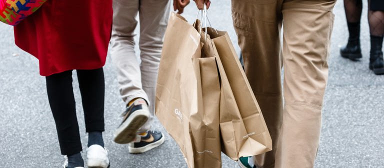 Beine von Menschen. Ein Mensch hält zwei Shoppingtüten in der Hand. (Foto: dpa Bildfunk, picture alliance/dpa | Markus Scholz)
