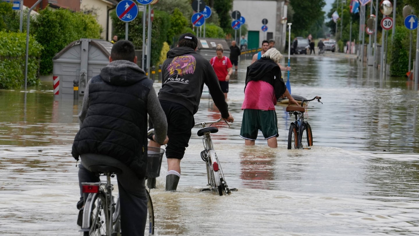 Ein Mann fährt auf einem Fahrrad eine überflutete Straße entlang. Die Region Emilia-Romagna kommt nach den Überschwemmungen nicht zur Ruhe. (Foto: dpa Bildfunk, picture alliance/dpa/AP | Luca Bruno)