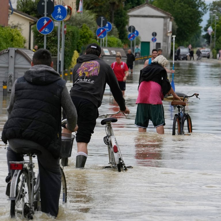 Ein Mann fährt auf einem Fahrrad eine überflutete Straße entlang. Die Region Emilia-Romagna kommt nach den Überschwemmungen nicht zur Ruhe. (Foto: dpa Bildfunk, picture alliance/dpa/AP | Luca Bruno)