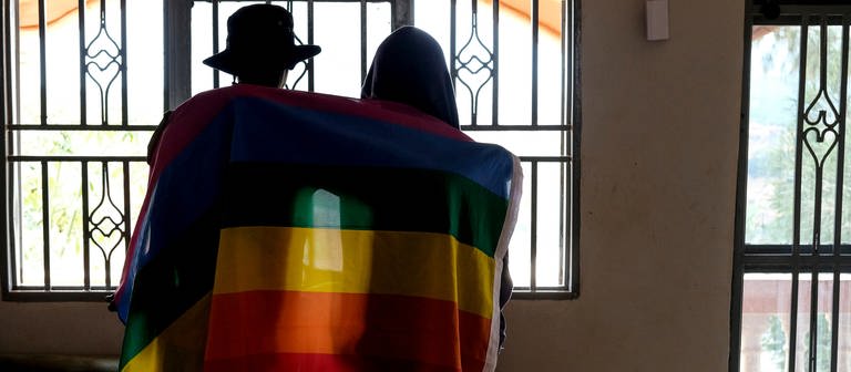 Ein Paar bedeckt sich mit einer Pride-Fahne. In Uganda hat das Parlament ein überarbeitetes Gesetz gegen Homosexuelle verabschiede (Foto: dpa Bildfunk, picture alliance/dpa/AP | Uncredited)