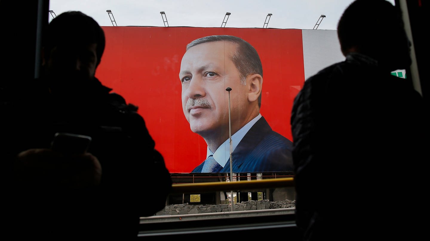 Die Silhouetten zweier Menschen vor einem Plakat von Staatspräsident Erdoga. - Ein 16-Jähriger wurde festgenommen weil er einen sogenannten Hitlerbart auf ein Erdogan-Plakat gemalt hat. (Foto: dpa Bildfunk, picture alliance / Emrah Gurel/AP/dpa | Emrah Gurel)