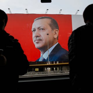 Die Silhouetten zweier Menschen vor einem Plakat von Staatspräsident Erdoga. - Ein 16-Jähriger wurde festgenommen weil er einen sogenannten Hitlerbart auf ein Erdogan-Plakat gemalt hat. (Foto: dpa Bildfunk, picture alliance / Emrah Gurel/AP/dpa | Emrah Gurel)