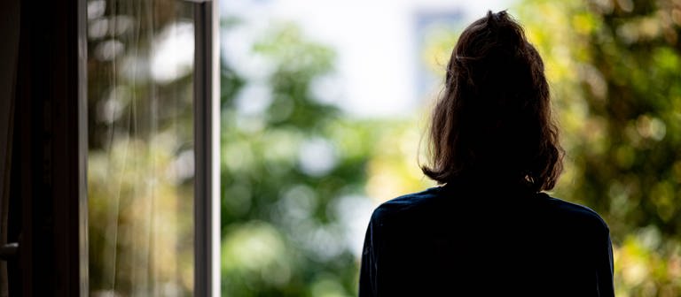 Frau steht am Fenster. Symbolbild für mentale Gesundheit (Foto: dpa Bildfunk, Picture Alliance)
