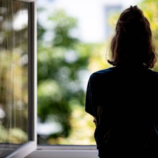 Frau steht am Fenster. Symbolbild für mentale Gesundheit (Foto: dpa Bildfunk, Picture Alliance)