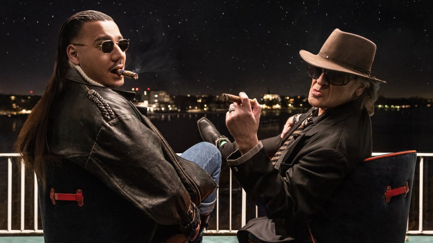 Rapper Apache 207 aus Ludwigshafen und Udo Lindenberg sitzen mit Zigarren nebeneinander auf einem Balkon und blicken in die Nacht (Foto: dpa Bildfunk, picture alliance/dpa/Warner Music | Tine Acke)