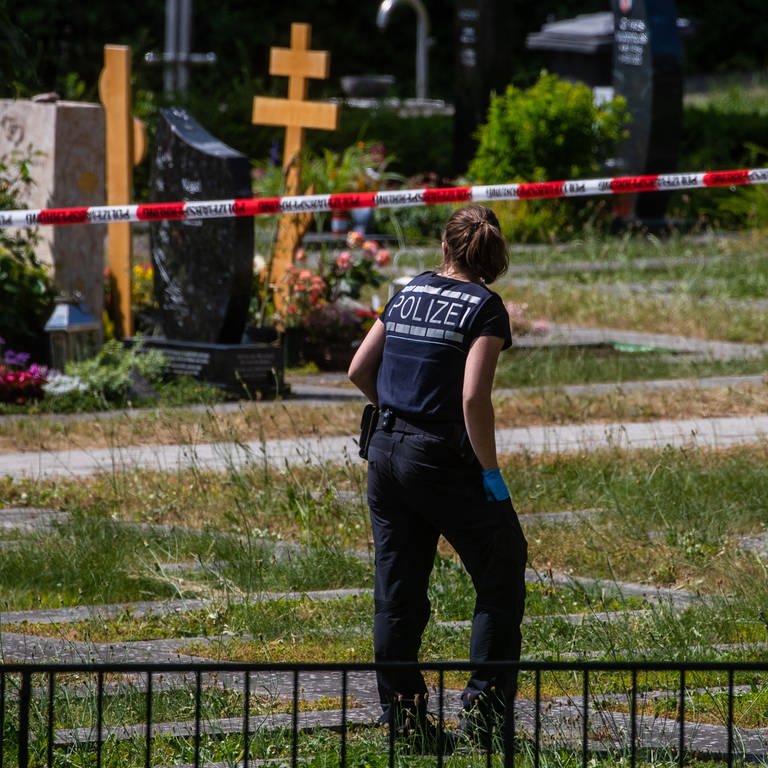 Eine Polizistin geht über den abgesperrten Teil an einem Tatort auf einem Friedhof. (Foto: dpa Bildfunk, picture alliance/dpa | Christoph Schmidt)