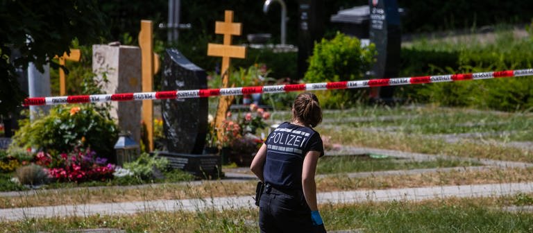 Eine Polizistin geht über den abgesperrten Teil an einem Tatort auf einem Friedhof. (Foto: dpa Bildfunk, picture alliance/dpa | Christoph Schmidt)