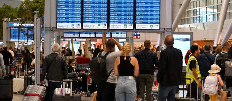 Passagiere stehen am Flughafen vor dem Flugplan. Trotz hoher Preise für Flugtickets reisen die Menschen im Sommer 2023 fast so viel wie 2019 vor der Corona-Pandemie. (Foto: dpa Bildfunk, picture alliance/dpa | Roberto Pfeil)