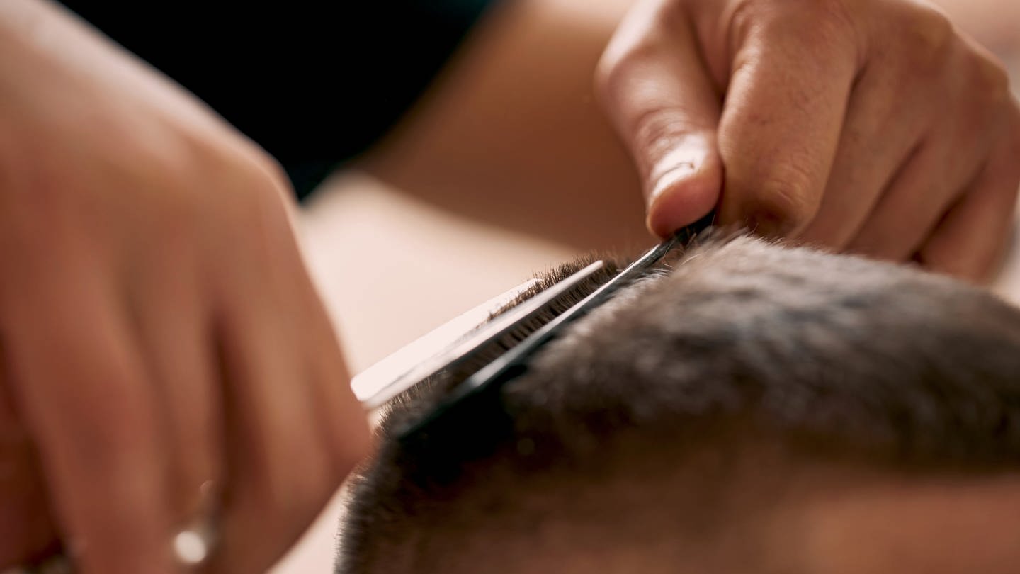 Ein Friseur schneidet einem Mann mit einer Schere die Haare. (Foto: IMAGO, Panthermedia)