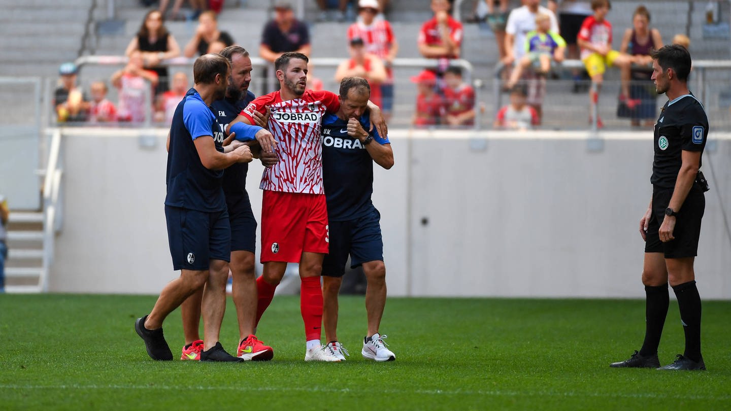 Christian Günter wird mit einem gebrochenen Arm vom Feld begleitet (Foto: IMAGO, IMAGO / Beautiful Sports)