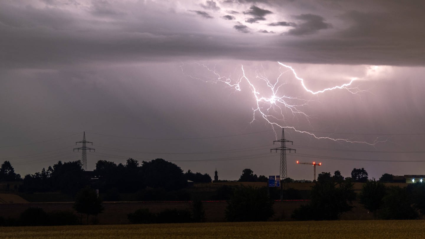 Ein Blitz ist hinter einem Strommast zu sehen. (Symbolbild) (Foto: IMAGO, Jan Eifert (Symbolbild))