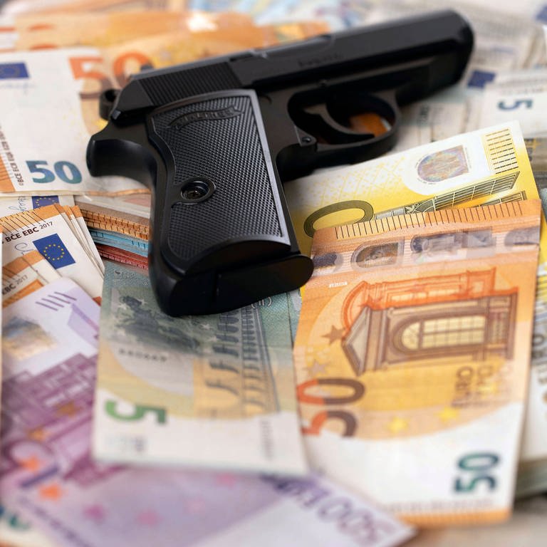 Eine Waffe bzw. Pistole liegt auf Geldscheinen. (Symbolbild) (Foto: IMAGO, IMAGO / Future Image)