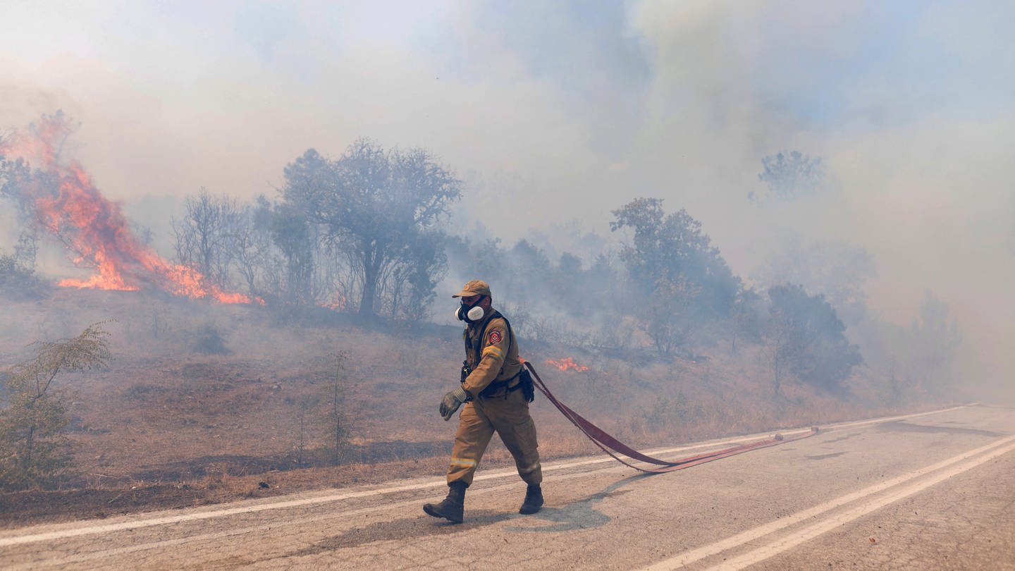 Ein Feuerwehrmann zieht einen Wasserschlauch bei Löscharbeiten während der Waldbrände in Griechenland. Dort wird jetzt wegen Brandstiftung ermittelt. (Foto: dpa Bildfunk, picture alliance/dpa/AP | Achilleas Chiras)