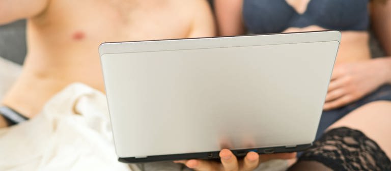 Amateur-Pornos und Ausbeutung - Paar liegt im Bett mit Laptop (Foto: IMAGO, IMAGO / Pond5 Images)