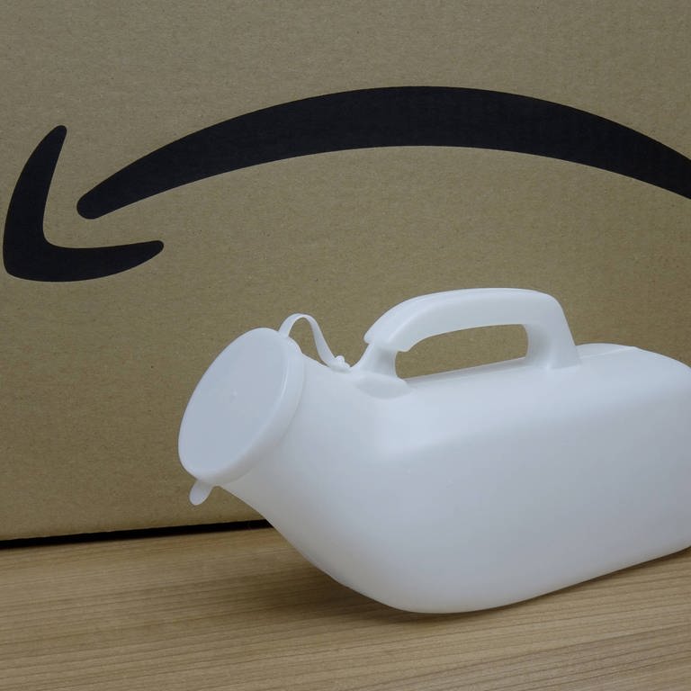 Vor einem Karton von Amazon steht eine Urinflasche. Immer wieder gibt es Kritik, dass Amazon-Fahrer keine Zeit für Pinkelpausen haben (Foto: IMAGO, IMAGO / Steinach)