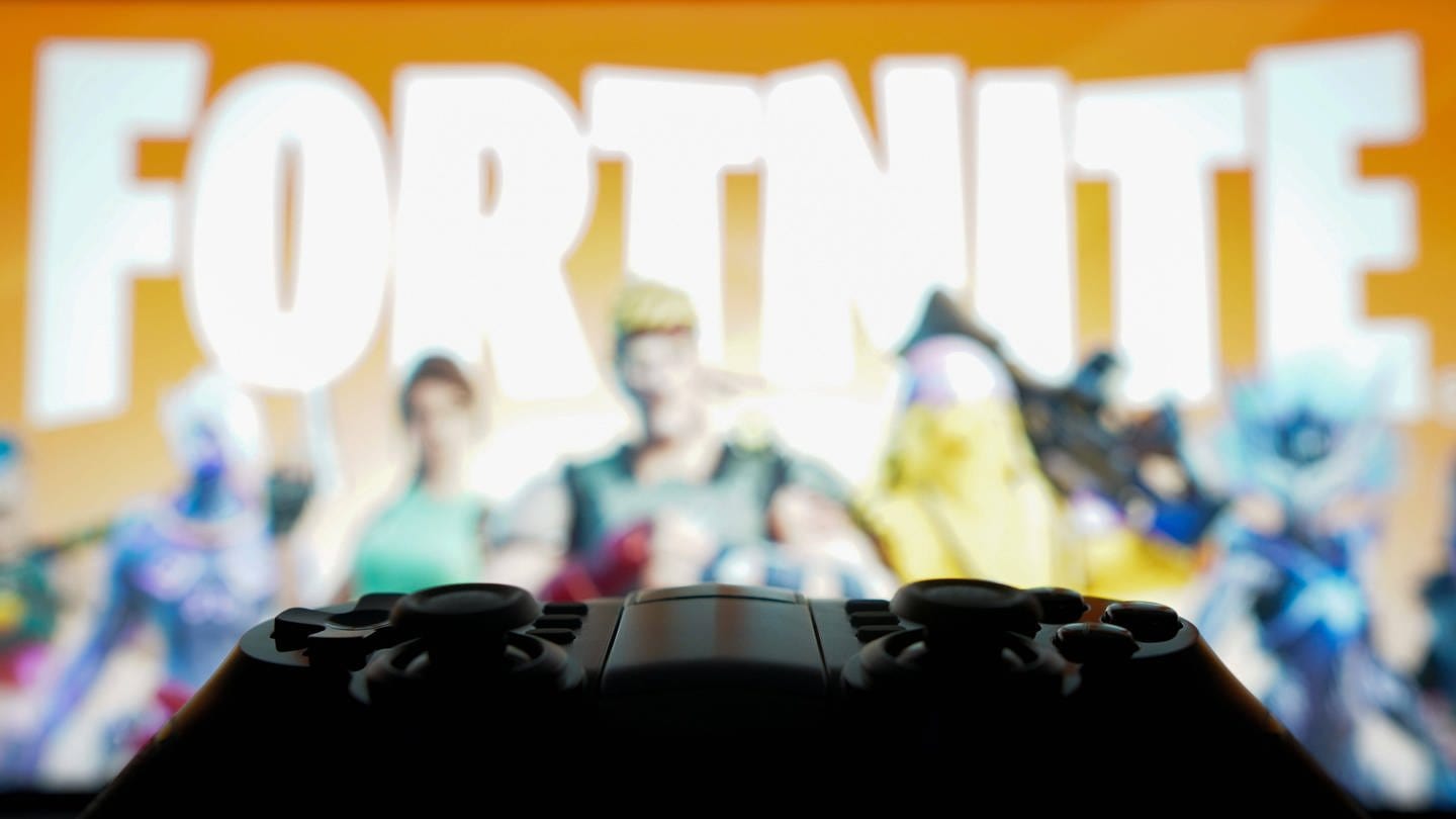 Spielkonsole und Fortnite-Screen im Hintergrund: Die neue Season Fortnite OG ist online - es ist eine Reise zu den Anfängen des Games. (Foto: IMAGO, IMAGO / SOPA Images)