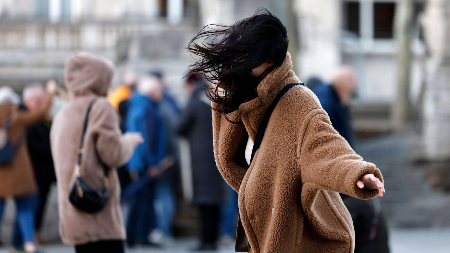 Frau auf der Straße wehen Haare ins Gesicht - über Baden-Württemberg soll am Wochenende ein Sturm ziehen. (Foto: IMAGO, IMAGO / Future Image)