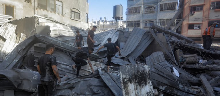Palästinenser und Mitarbeiter des Zivilschutzes suchen in den Trümmern eines zerstörten Gebäudes nach einem israelischen Luftangriff auf Chan Junis nach Überlebenden. (Foto: dpa Bildfunk, picture alliance/dpa | Mohammed Talatene)