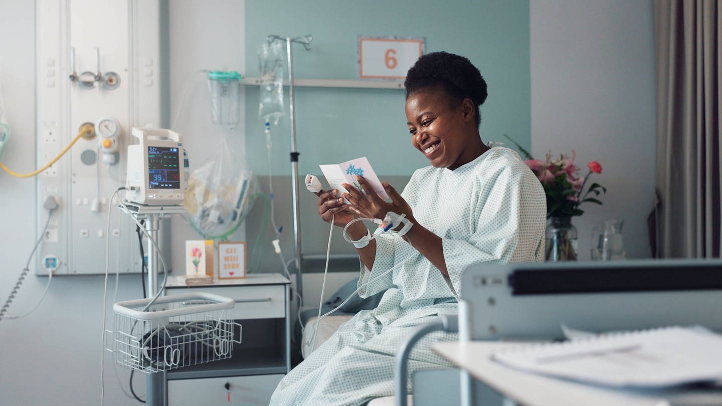 Symbolbild: Frau in Krankenhaus in OP-Kleidung lächelt und liest eine Karte. (Foto: IMAGO, IMAGO / Zoonar II (Symbolbild))