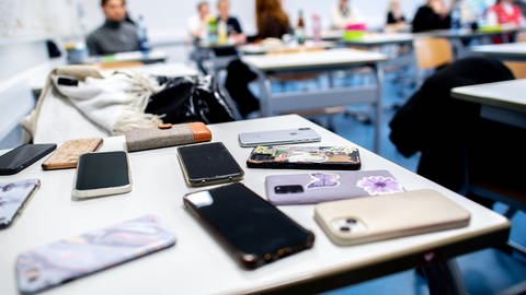 picture alliancedpa | Hauke-Christian Dittrich (Foto: dpa Bildfunk, Handys liegen im Klassenzimmer auf dem Tisch: Neuseeland will Handys an Schulen verbieten)