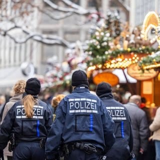 Polizisten von hinten auf dem Weihnachtsmarkt in Stuttgart: Polizei will ihre Präsenz erhöhen nach dem Anschlagspläne bekannt wurden.  (Foto: IMAGO, IMAGO / Arnulf Hettrich)