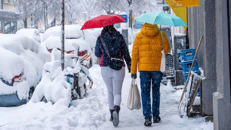 Zwei Menschen laufen mit Regenschirmen durch den tiefen Schnee in der Stadt. Der Schneefall ist aber kein Zeichen gegen den Klimawandel.  (Foto: IMAGO, IMAGO / Wolfgang Maria Weber)