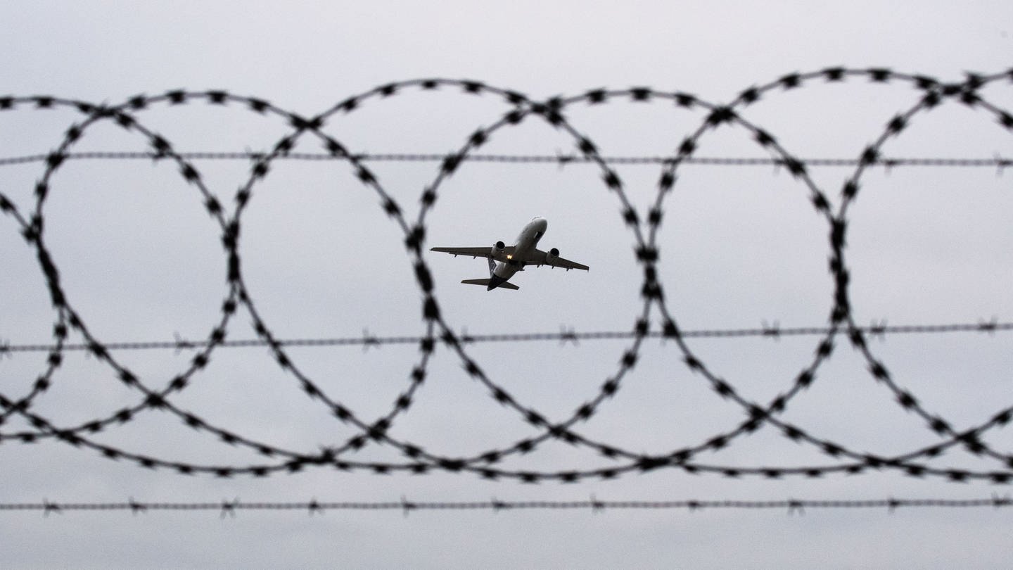 Ein Flugzeug startet - fotografiert durch Stacheldraht am Flughafenzaun. (Foto: dpa Bildfunk, picture alliance/dpa | Julian Stratenschulte)