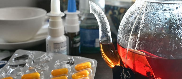 Medikamente und eine Kanne und Tasse Tee zur Bekämpfung einer Erkältung sind auf einem Nachttisch aufgestellt. (Foto: dpa Bildfunk, picture alliance/dpa | Bernd Weißbrod)