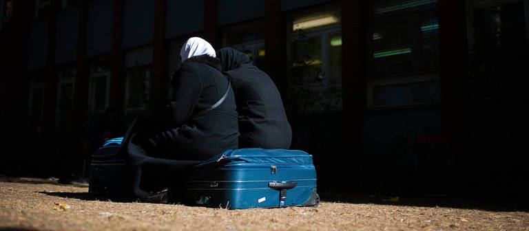 Zwei Frauen sitzen auf ihren Gepäckstücken. (Foto: IMAGO, IMAGO / photothek)