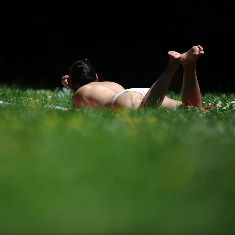 Frau liegt oben ohne im Park und sonnt sich: Ein Gerichtsurteil erlaubt Frauen in Berlin jetzt auch auf einem Wasserspielplatz ihre Brüste zu zeigen. (Foto: dpa Bildfunk, picture alliance / dpa | Andreas Gebert)
