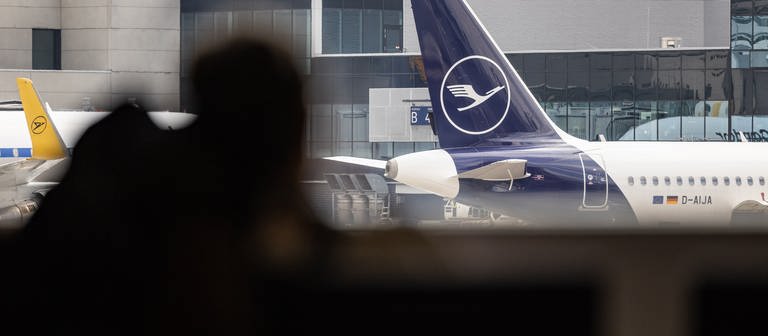 Blick auf das Heck einer Lufthansa Maschine, im Vordergrund sind zwei Personen. - Am Mittwoch will das Bodenpersonal der Lufthansa streiken. (Foto: dpa Bildfunk, picture alliance/dpa | Hannes P Albert)