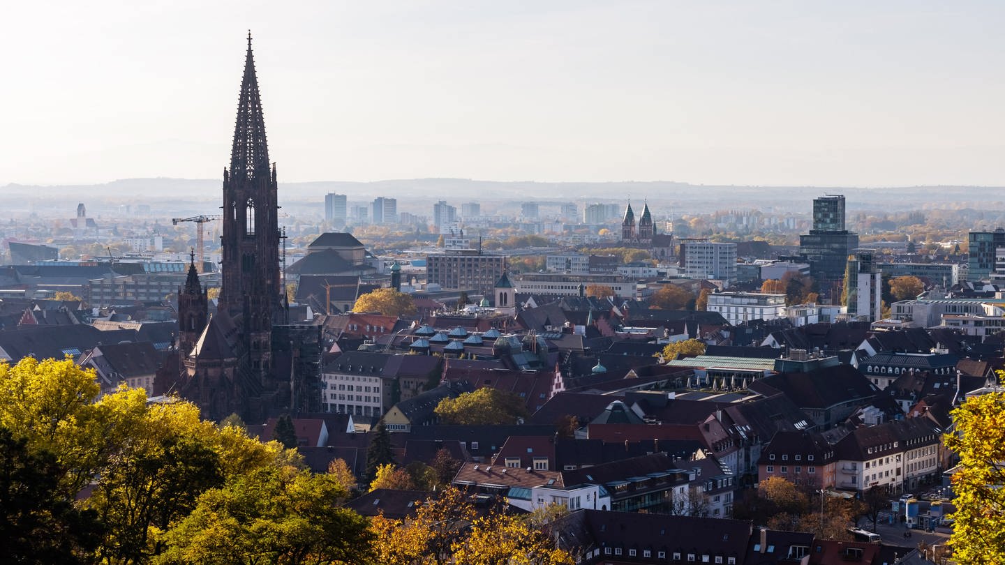 Der Turm des Freiburger Münsters ragt über die Dächer der Innenstadt hinaus, während im Hintergrund Hochhäuser im Stadtteil Weingarten und die Rheinebene zu sehen sind. - In Freiburg wird ein Konsumraum eröffnet. Die Polizei warnt, dass die Stadt von Kokain und Crack 