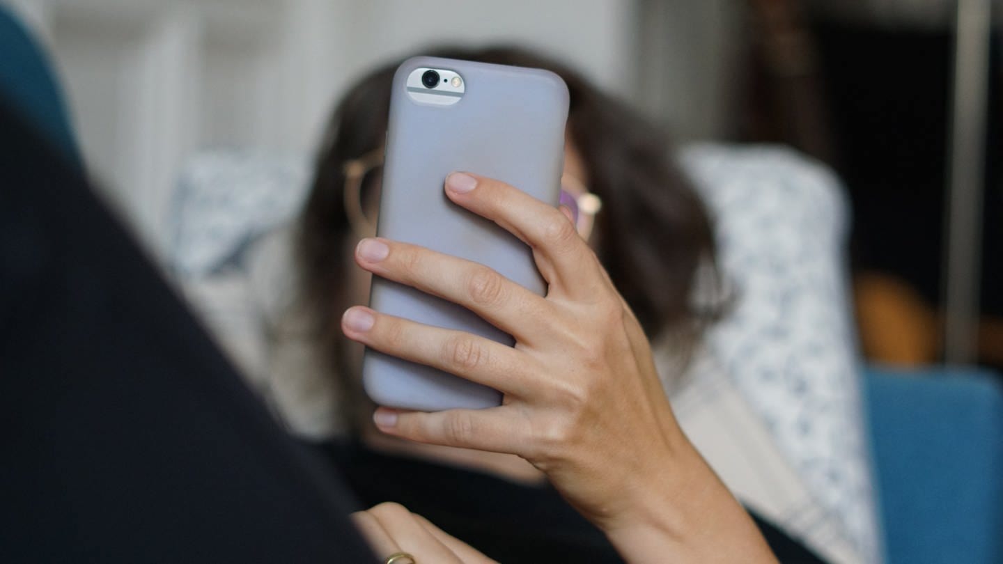 Eine Frau liegt auf einem Sofa und schaut auf ihr Handy - Ab heute gelten in der EU strengere Regeln. WhatsApp, Apple, Google, Amazon und Tiktok sollen so weniger Macht haben. (Foto: dpa Bildfunk, picture alliance/dpa | Weronika Peneshko)