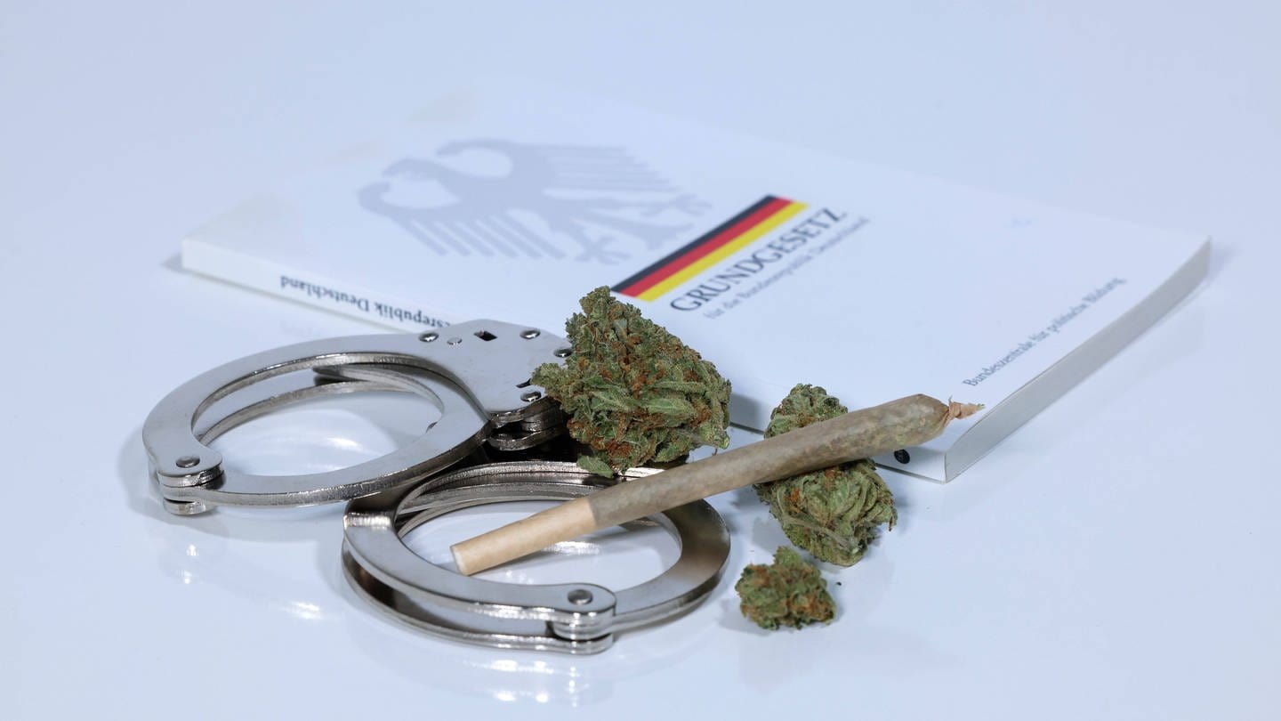 Ein Buch mit dem Grundgesetz, Handschellen und Cannabis. (Foto: IMAGO, IMAGO / Revierfoto)