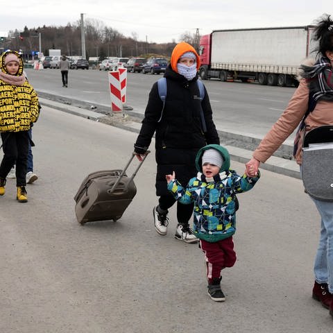 An einer Straße gehen Flüchtlinge aus der Ukraine entlang, es sind Frauen und Kinder.