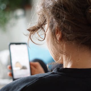 Eine Frau liegt auf einem Sofa und schaut sich ein Video auf Instagram auf ihrem Handy an. (Foto: dpa Bildfunk, picture alliance/dpa | Weronika Peneshko)
