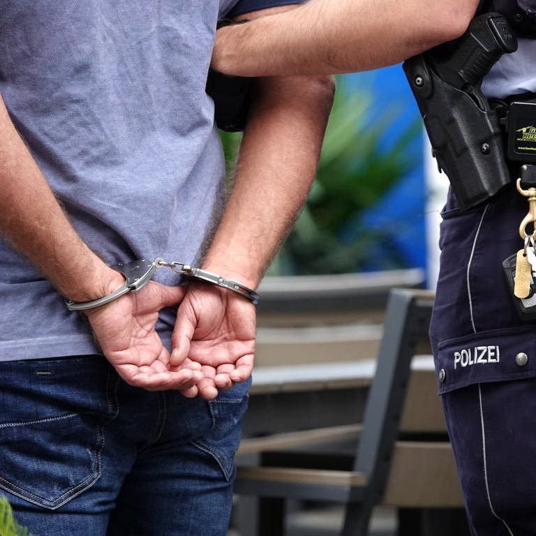 Ein Mann ist mit Handschellen auf den Rücken gefsselt und wird von einem Polizisten festgehalten. (Foto: dpa Bildfunk, picture alliance/dpa | Johannes Neudecker)