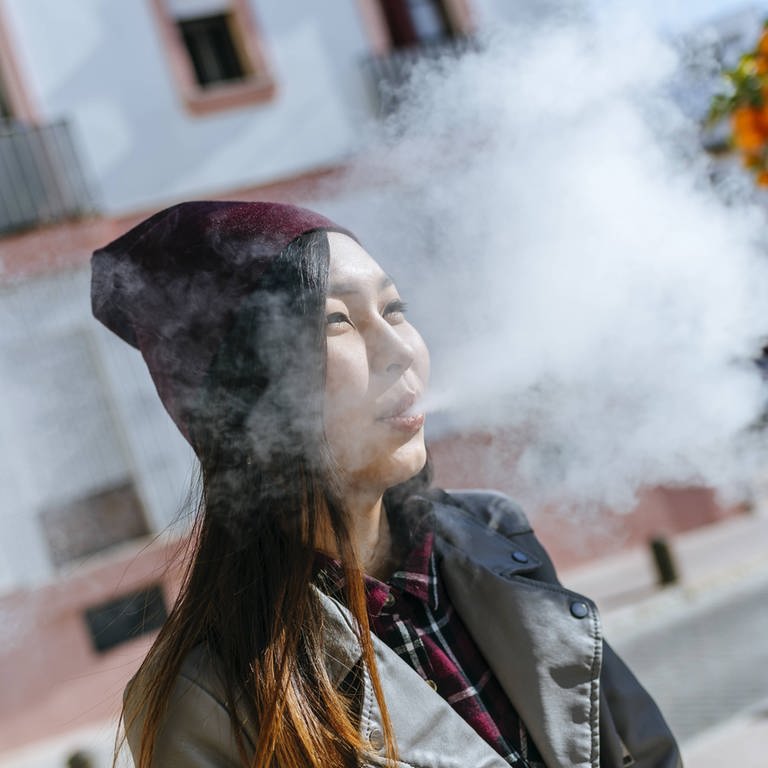 Young woman blowing out smoke from electronic cigarette model released Symbolfoto