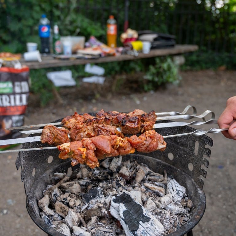 Ein Mann grillt im Park auf einem Grillplatz Fleischspieße.